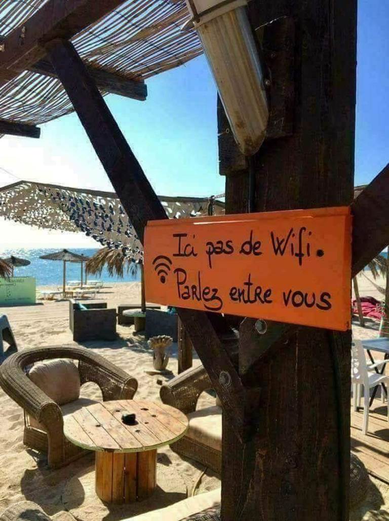 Un bar de plage, du sable, des chaises et des tables, et une simple affiche "Ici, pas de wifi : parlez entre vous !"
Image prise en Corse et partagée par des Internautes